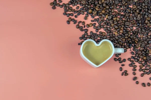 A mug of invigorating black coffee with heart-shaped foam and coffee beans on a pink background. Place for an inscription. Concept of hot drinks and love.