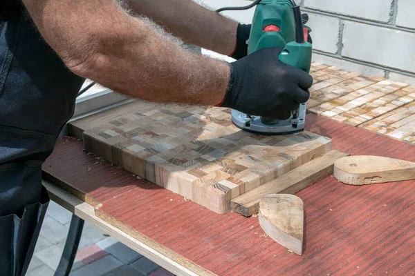 A carpenter at a hand-held hand-held milling machine in a carpentry workshop. End cutting boards. Joiner.