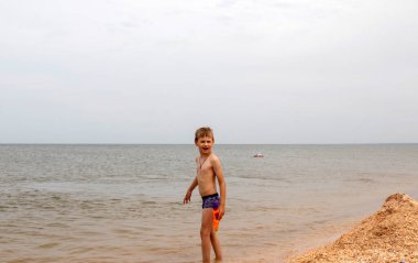 Çocuk yaz tatilinde plajda oynuyor. Doğada çocuklar ve güzel bir deniz. Mutlu çocuk denizde tatilde, suda koşuyor.