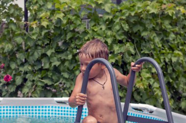 Evin yakınındaki havuzda çocuklar yüzüyor ve keyif alıyorlar. İki kardeş havuzda yüzüyorlar. Mavi su ve parlak yüzme çemberleri. Eğlence, kahkaha ve yaz.