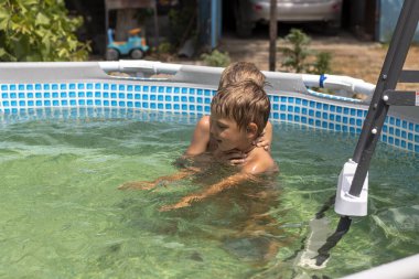 Çocuk çerçeve havuzunda yüzer ve güler. Yaz güneşli bir gün. Mavi ve ılık havuz suyu.