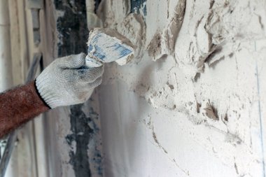 İnşaatçı alçıtaşı alçısıyla duvarı düzleştiriyor. Adam tamir sırasında düzensizlikleri dikkatlice düzeltir..