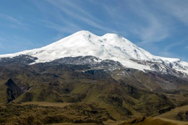 Ufuktaki kar kaplı dev Elbrus dağları mavi gökyüzüne karşı. Kafkas Dağları 'nın dağlık, tepelik yaz manzarası