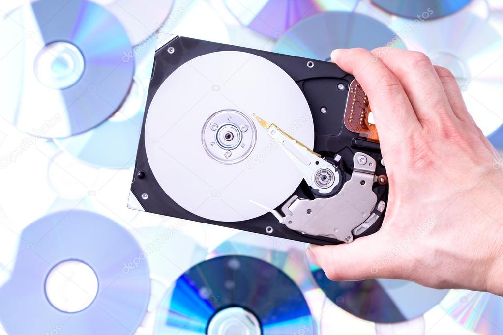 Man's hand with hard disk drive over CD's background. Concept of