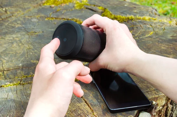 Woman is connecting her smartphone with wireless speaker while being outdoor. — Stock Photo, Image