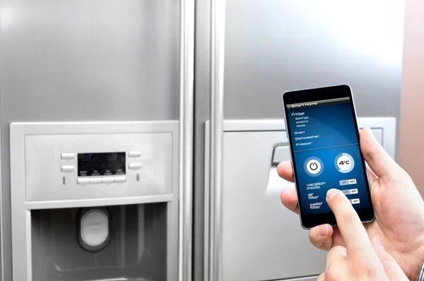 Man uses his smartphone to set up the fridge — Stock Photo, Image