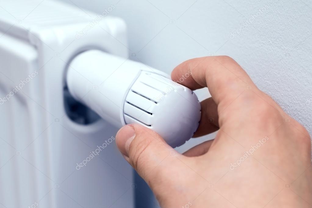 Man's hand adjusting radiator temperature.