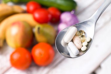 Gümüş kaşıkla meyveli arka plan üzerinde diyet takviyeleri