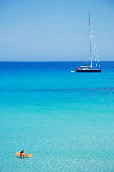 Mallorca, Balearen, Spanien: ein Segelboot und zwei kleine Mädchen mit einer gelben Luftmatratze am Strand von Cala Torta, einem der unbewohnten Strände im Nordosten der Insel — Stockfoto