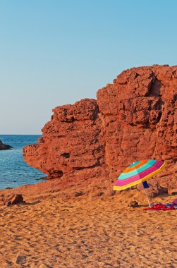 Menorca, Balear Adaları: Cala Pregonda bir plaj şemsiyesi, kırmızı kum ve kayalar