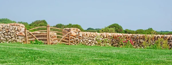 Menorca, Islas Baleares: muro de piedra, puerta de madera y césped en la campiña menorquina — Foto de Stock