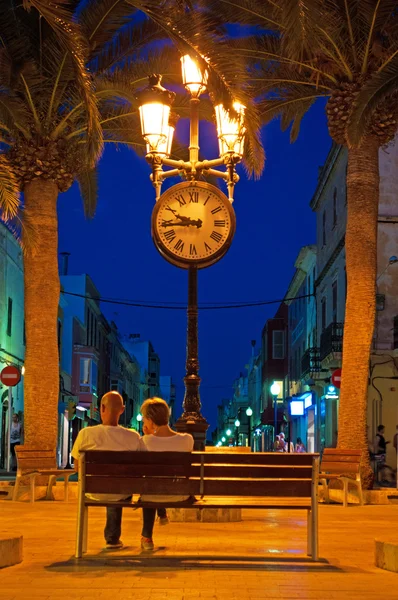 Menorca, Ilhas Baleares: skyline noite de Ciutadella de Menorca com vista para um casal em um banco na praça da cidade de Placa d 'Alfons III — Fotografia de Stock