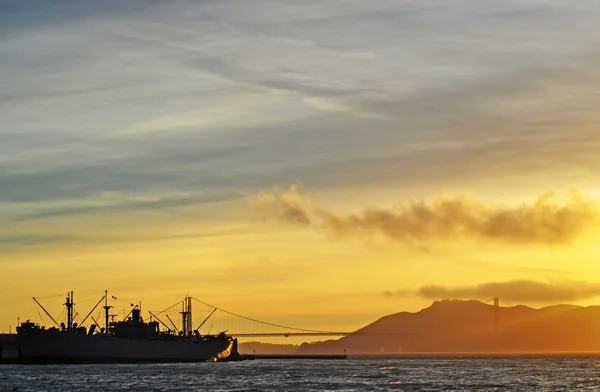 San Francisco, Kalifornien, Usa: Fisherman's Wharf, ett skepp och utsikt över solnedgången på Golden Gate-bron sedd från den berömda piren 39 — Stockfoto