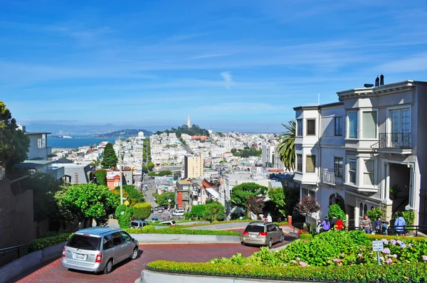 San Francisco, California: horizonte y coches en la calle de Lombard Street, east-west famoso por una sección de un bloque fuerte con horquilla de ocho vueltas, famosa a ser una de las calles más torcidas del mundo — Foto de Stock