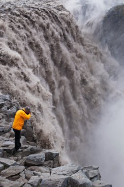 Iceland, Europe: a man taking pictures of Dettifoss, the waterfall in Vatnajokull National Park, one of the most powerful waterfall in Europe and main icelandic tourist destination, famous for its alien surrounding landscape