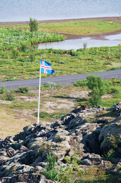 Islândia, Europa: Logberg, a rocha da lei, centro da reunião de Althing, Parlamento nacional de 930 dC a 1798, com uma bandeira islandesa no parque nacional Thingvellir, um vale que marca a fronteira entre placas tectônicas norte-americanas e eurasianas — Fotografia de Stock