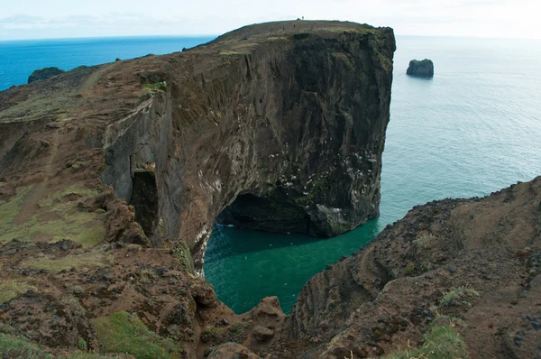 Islandia, Europa: vista aérea del gigantesco arco negro de lava que se encuentra en el mar sobre el promontorio de Dyrholaey y con vistas a la bahía de Vik i Myrdal, el pueblo más al sur de la isla, uno de los principales atractivos turísticos del sur —  Fotos de Stock