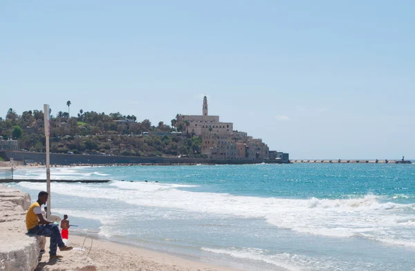 Tel Aviv, Israele, Medio Oriente: un uomo sulla spiaggia e la vista panoramica dello skyline della città vecchia di Jaffa con il campanile della chiesa di San Pietro, una chiesa francescana costruita nel 1654 sulla cima della parte più antica di Tel Aviv Yafo — Foto Stock