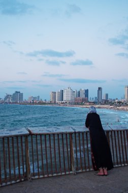 Tel Aviv, Israel, Middle East: a muslim woman at the promenade of Jaffa, the oldest part of Tel Aviv Yafo in which Arabs and Jews live together, with view of the Mediterranean Sea and the modern skyline of Tel Aviv clipart