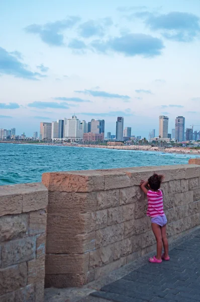 Tel Aviv, Israel, Middle East: a muslim child playing hide and seek on the stone wall of the promenade of Jaffa, the oldest part of Tel Aviv Yafo, with view of the Mediterranean Sea and the modern skyline of Tel Aviv