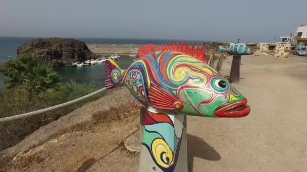 El Cotillo, Fuerteventura, Kanári-szigetek, Spanyolország, 2016. augusztus 29.: A parton, a falu El Cotillo kikötő és a Castillo de El Cotillo áttekintése. Szobrászat, a festészet hal. — Stock videók