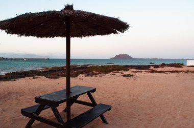 Fuerteventura, Kanarya Adaları, İspanya: ahşap masa, plaj şemsiyesi ve Lobos Adası (Islote de Lobos) görünümünü, küçük bir ada 2 kilometre Corralejo bir plaj görülen Fuerteventura Adası kuzeyinde yer alan