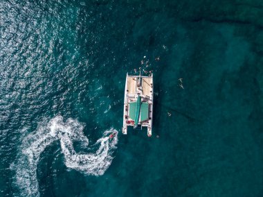 Kanarya, İspanya 'nın Lanzarote adasının kıyıları yakınlarında, içinde insan bulunan ve denizde yüzen katamaranın havadan görünüşü. Jet ski denizde gösteri yapıyor.