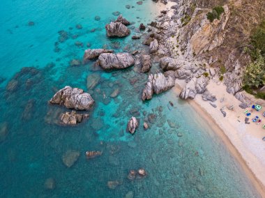 Plajın ve şemsiyelerin havadan görünüşü. Tropea, Calabria, İtalya. Parghelia. Yukarıdan görünen deniz yatağının genel görünümü, şeffaf su. Yüzücüler, suda yüzen banyocular. Vardanello sahilleri ve kayalıkları
