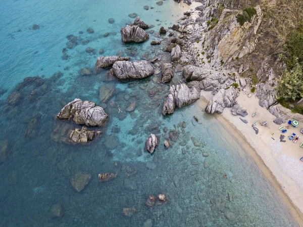 Aerial view of a beach and umbrellas. Tropea, Calabria, Italy. Parghelia. Overview of seabed seen from above, transparent water. Swimmers, bathers floating on the water. Beach and rocks of Vardanello — Stock Image Aerial View Beach Umbrellas Tropea Calabria Italy Parghelia Overview Seabed Royalty Free Stock Images