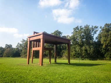 Monza Parkı 'ndaki Giancarlo Neri' nin yazarı. 10-17-2020. Sandalye ve masa, parkın yeşilliğiyle çevrili bir sanat kurulumu uyum içinde, çevresindeki doğayla bir bağlantı oluşturuyor.