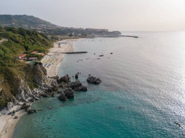 Plajın ve şemsiyelerin havadan görünüşü. Tropea, Calabria, İtalya. Parghelia. Yukarıdan görünen deniz yatağının genel görünümü, şeffaf su. Yüzücüler, suda yüzen banyocular. Vardanello sahilleri ve kayalıkları