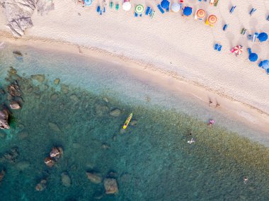 Plajın ve şemsiyelerin havadan görünüşü. Tropea, Calabria, İtalya. Parghelia. Yukarıdan görünen deniz yatağının genel görünümü, şeffaf su. Yüzücüler, suda yüzen banyocular. Vardanello sahilleri ve kayalıkları