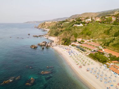 Plajın ve şemsiyelerin havadan görünüşü. Tropea, Calabria, İtalya. Parghelia. Yukarıdan görünen deniz yatağının genel görünümü, şeffaf su. Yüzücüler, suda yüzen banyocular. Vardanello sahilleri ve kayalıkları