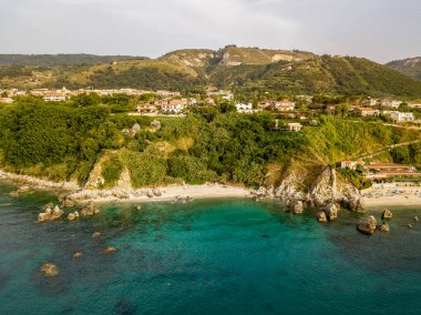 Plajın ve şemsiyelerin havadan görünüşü. Tropea, Calabria, İtalya. Parghelia. Yukarıdan görünen deniz yatağının genel görünümü, şeffaf su. Yüzücüler, suda yüzen banyocular. Vardanello sahilleri ve kayalıkları