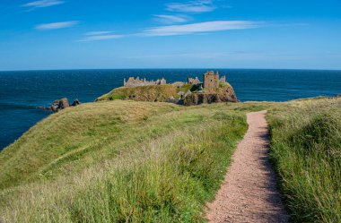 Stonehaven, Aberdeenshire, İskoçya, Birleşik Krallık: Dunnottar Şatosu 'ndaki çimlerin üzerindeki patika manzarası, kuzeydoğu kıyısındaki kayalık bir burundaki yıkık ortaçağ kalesi.