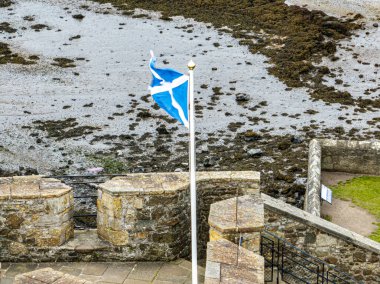 Karanlık Kale 'nin üzerinde dalgalanan İskoç bayrağının hava görüntüsü. Firth of Forth 'un güney kıyısında 15. yüzyıldan kalma bir kale. Outlander dizisinin seti