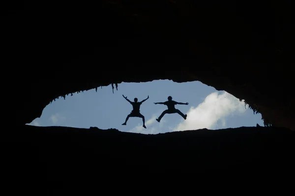 Sokotra, Jemen, Naher Osten: die Silhouette zweier Männer, die am Eingang der Hoq-Höhle springen, dem geschützten Gebiet der Homhil-Hochebene auf der Insel Sokotra, seit 2008 Unesco-Weltnaturerbe wegen ihrer Artenvielfalt — Stockfoto