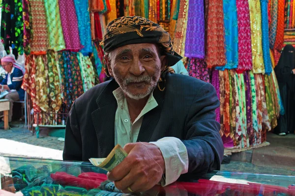 Yemen, Middle East: a yemeni old man with turban paying after shopped at the fabric store in Suq al-Milh, the salt market of Sana'a, capital of the country, the oldest continuously inhabited and populated city in the world, — Stock Photo, Image
