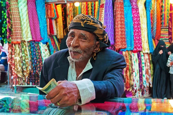 Yemen, Middle East: a yemeni old man with turban paying after shopped at the fabric store in Suq al-Milh, the salt market of Sana'a, capital of the country, the oldest continuously inhabited and populated city in the world,