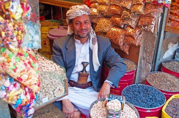 Yemen, Middle East: a yemeni man, seated at the entrance of his shop, selling candies, dried fruit, cereals and spices in Suq al-Milh, the salt market of the old town of Sana'a — Stock Photo, Image