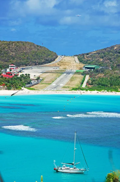 Saint Barthelemy (St Barth, St. Barths o St. Barts): la vegetazione con la famosa spiaggia di Saint Jean e la pista di atterraggio dell'aeroporto Gustaf III con una barca a vela nella baia — Foto Stock