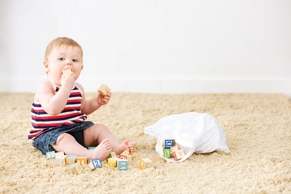 Baby: Liten flicka leker med leksak träklossar på mattan — Stockfoto