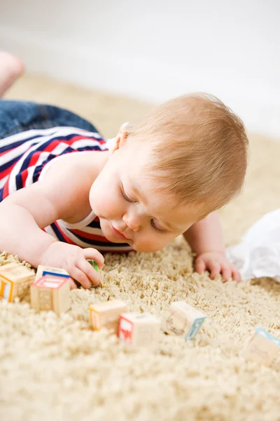 Baby: Liten flicka leker med leksak träklossar på mattan — Stockfoto