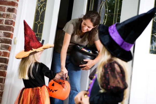 Halloween: Las manos de la madre fuera de caramelo a la bruja niña — Foto de Stock