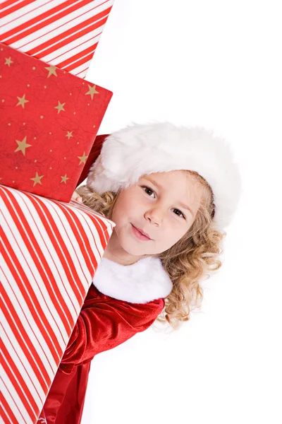 Natal: bonito Santa menina espreita em torno de pilha de presentes — Fotografia de Stock