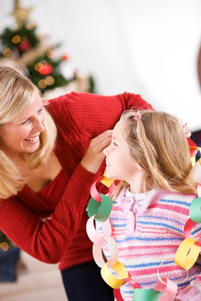 Kerstmis: Moeder Wraps papier keten Garland rond meisje — Stockfoto