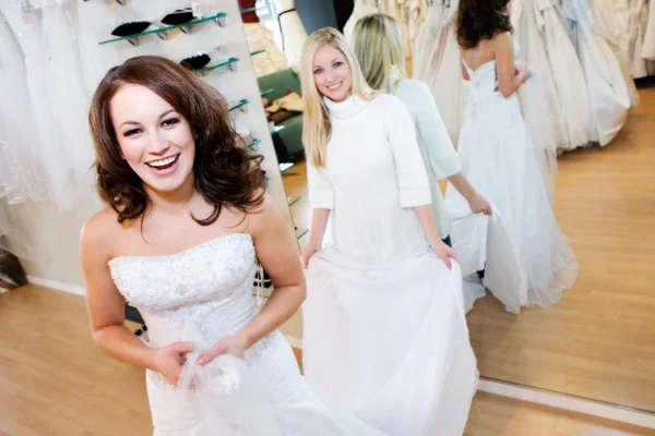 Noiva: Mulher tentando no vestido de casamento com a ajuda da vendedora — Fotografia de Stock