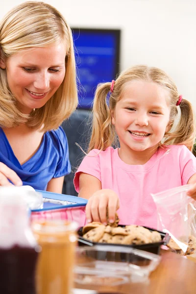 学生: 女の子と母親は、学校給食に最後の仕上げを置きます。 — ストック写真