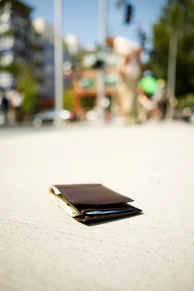 Geldbörse: Geldbörse auf Gehweg, während Mann im Hintergrund Tasche checkt — Stockfoto