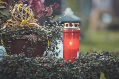 Mezarlıktaki bir mezara kırmızı mum yakın.